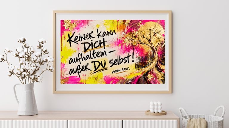 Bunte Wandkunst im Wohnzimmer mit dem Schriftzug 'Keiner kann dich aufhalten außer du selbst!' neben einem abstrakten Baum in Gelb- und Pinktönen. Das Bild hängt über einem weißen Sideboard mit Baumwollblumen in einer weißen Vase.
